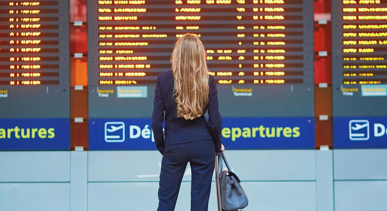 Compensación a pasajeros por gran retraso de un vuelo con conexión directa objeto de una reserva única. Imagen de una mujer en un aeropuerto mirando las pantallas de los vuelos