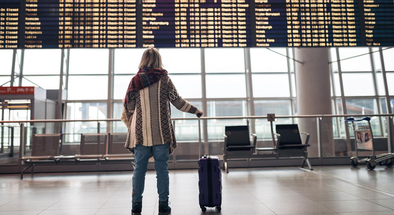 Adelanto de vuelo contratado a través de una plataforma electrónica. Comunicación al pasajero. Imagen de una chica viendo las pantallas donde aparecen los vuelos en el aeropuerto